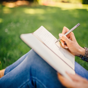 woman writing in notebook on the grass